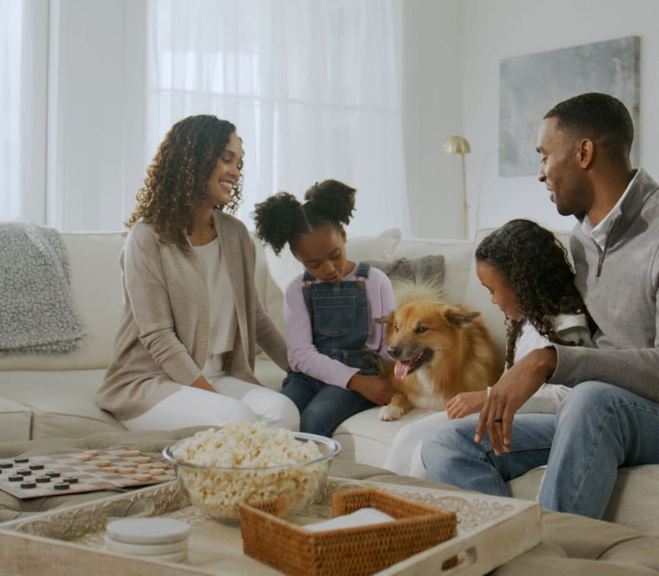 APlusFamilyHero-960×840 Family sitting on a couch with a dog